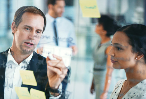 Shot of two businesspeople brainstorming with notes on a glass wall in an office